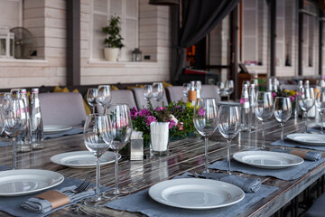Modern veranda restaurant interior, flowers, banquet setting, glasses, plates