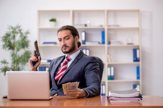 Young male employee holding gun and banknotes in bankruptcy conc