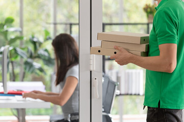 A young boy food delivery sender holding pizza paper boxes arrives at the customer's office and...