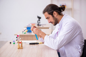 Young male chemist sitting at the desk in the classroom