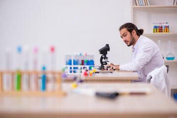 Young male chemist sitting at the desk in the classroom