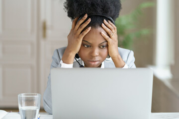 Portrait of tired annoyed afro businesswoman, wear headphones, talking to a bad customer looking at...