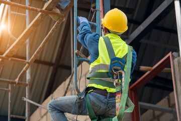 Construction worker wearing safety harness belt during working on a scaffold at house under construction.