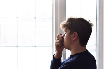 Young man using puffer inhaler to control his asthma 