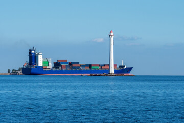 Ship is loaded with sea containers. Cargo tanker next to the lighthouse. Cargo ship drives past...