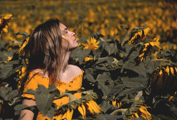 Young girl in a sunflower field with her face towards the sun