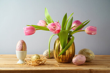 Easter holiday concept with beautiful tulip flowers, pink and golden eggs on wooden table