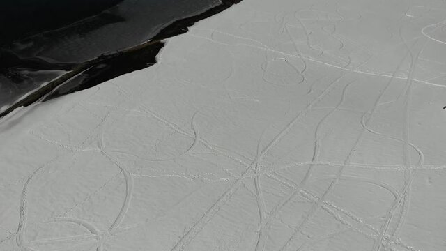 Drone flight abstract texture people and snowmobile tracks crisscross fresh snow field 