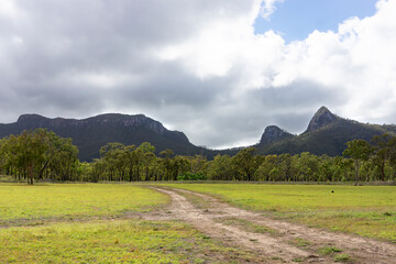 Early morning landscape with mountains and escarpments rising from a green field with a gravel path at the historical abandoned mining town of Mount Britton, Central Queensland, Australia.