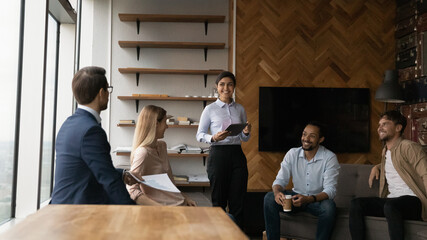 Successful multiethnic business team sharing experience discuss project sales strategy at informal briefing. Young indian female hold tablet pc speak on staff meeting training in friendly atmosphere