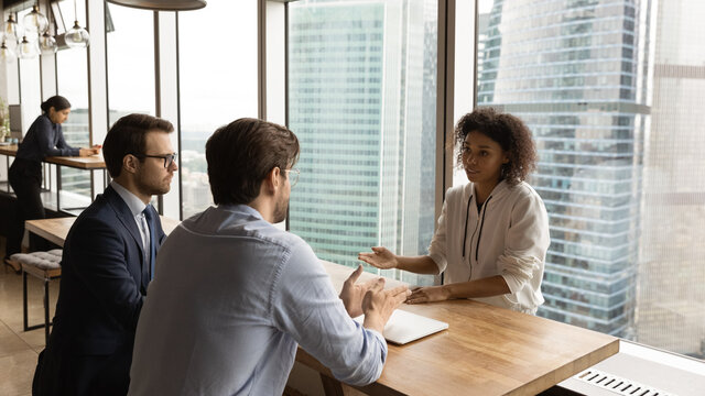 Two male recruiters interviewing young african american female job seeker in modern open space office. Concentrated black woman applicant answer hr managers questions about professional experience