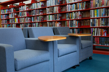 A row with 3 upholstered chairs with tablet swivel arm and red bookshelf with books in background