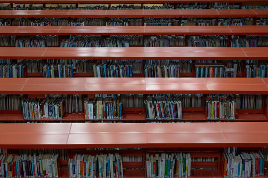 A slight topside, frontal view of rows of tall red metal bookshelves with books