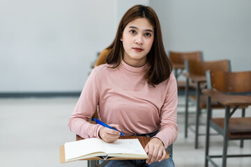 Young woman college students sitting on lecture chair in classroom studying, writing on examination paper answer sheet in doing the final examination test. College students in the classroom