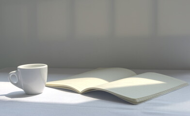 An open notebook and white coffee cup on the table under sunlight