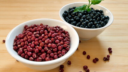Closeup of a bowl of adzuki beans and a bowl of black beans on wooden table