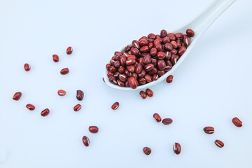 Closeup of a spoon of dry raw red adzuki beans, some scattered on background