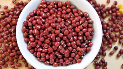 Top view of adzuki beans in a white bowl and some scattered on table