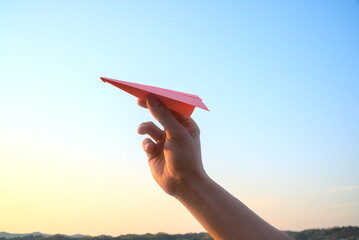 Hand holding a pink paper airplane on sunrise sky background