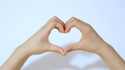 Fototapeta premium Female hands in the form of heart on white background under light.