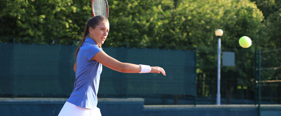 Professional equipped female tennis player beating hard the tennis ball with racquet.