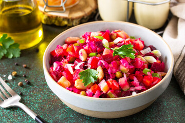 Beetroot salad vinaigrette close-up with pickled cucumber, beans, carrots, peas, sauerkraut on a dark countertop.
