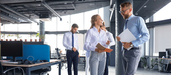 Group of modern business people are talking and smiling while standing in the office hallway