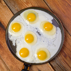 Fried eggs in a frying pan on an old rustic wooden table, top view.