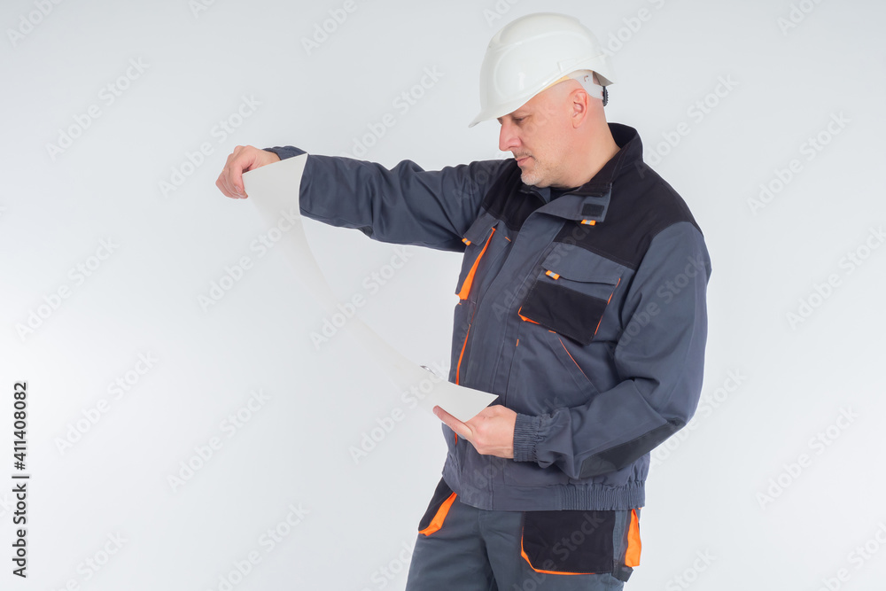 Poster portrait of engineer on a light background. engineer man in a gray uniform. he examines a piece of p