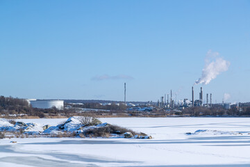 Fototapeta premium Frozen sea on a sunny winter day with chemical plants in the background. Gothenburg, Sweden 020621
