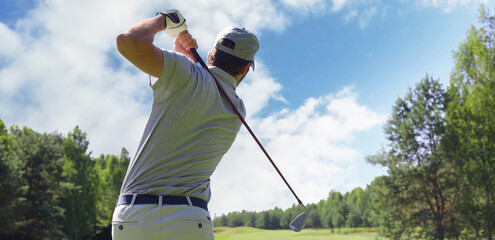 Golfer hitting golf shot with club on course while on summer vacation.