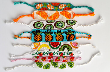 Woven DIY friendship bracelets handmade of embroidery bright thread with knots isolated on white background. Fruit alpha patterns