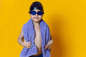 child athlete wearing blue swimming goggles and a black rubber cap stands in the studio on a yellow...