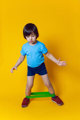 boy athlete does gymnastics with an elastic band in a sports club on a yellow background