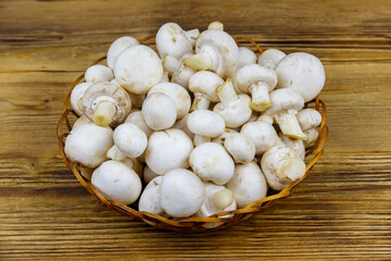Fresh champignon mushrooms in wicker basket on the wooden table