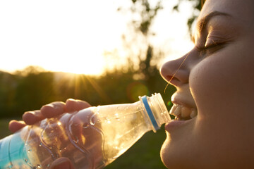 woman drinks water from a plastic bottle outdoors in summer