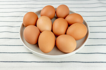 Closeup view of ceramics plate full of many raw whole brown chicken eggs on textile background