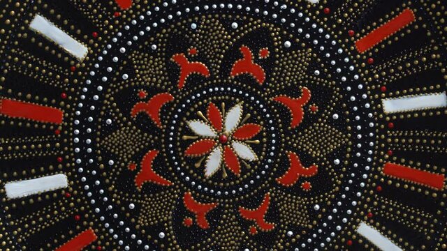 Decorative ceramic plate with red and golden colors, painted plate is rotating on background, close up, top view. Decorative porcelain plate painted with acrylic paints, handwork, dot painting