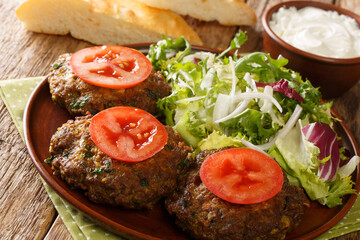 Spicy Indian Chapli Kebabs with fresh vegetables close up in the plate on the table. Horizontal