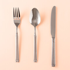 Spoon, fork and knife on a pastel peach-colored base. Flat lay.
