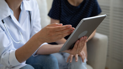 Crop close up of woman doctor or nurse and patient use look at tablet screen discuss consider analysis results. Female GP and client hold pad device analyze treatment in clinic. Recovery concept.