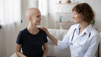 Smiling Caucasian doctor talk consult optimistic young hairless female cancer patient at home or...