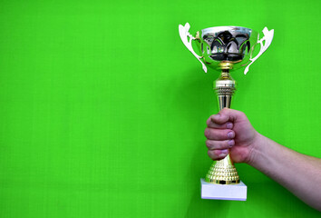 Sports cup in a man's hand on a green background. Champion golden trophy cup. Cup sport after a...