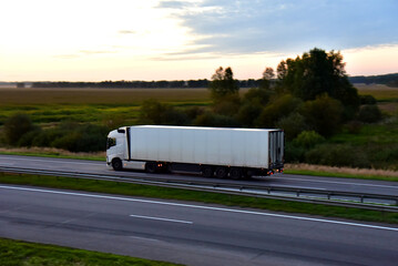 Truck with semi-trailer driving along highway on the sunset background. Goods delivery by roads. Services and Transport logistics. Soft focus. Object in motion.