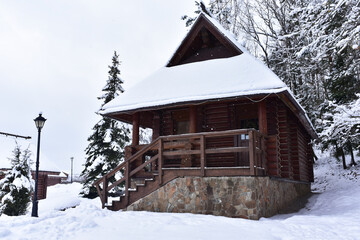 Wooden house in mountain in winter time. Log cabin in forest alone in wilderness. Wooden house with a wooden roof against background of snow-covered fir trees. Relaxation and solitude in wild