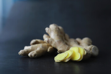 Ginger root whole and sliced. Ginger tea with lemon on the dark background. Fresh ginger root on stone background. Vitamins. Free space for your text.
