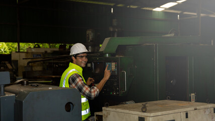 Mechanical engineer or worker with hardhat or helmet and safety uniform is checking heavy machine in a factory