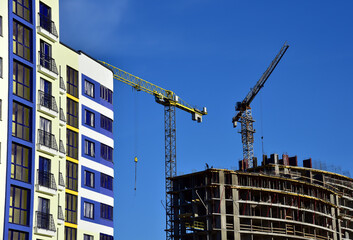 Tower cranes in action on blue sky background. Construction of new multi-storey buildings. Residential building is being constructed use of crane. Pouring of concrete in formwork