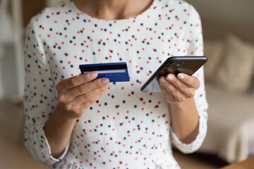 Crop close up of woman hold cellphone and credit card shopping make payment online using gadget. Female buyer or client pay bills or taxes on smartphone with secure banking system on device.