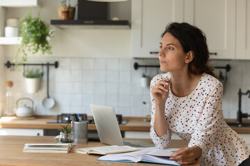 Pensive millennial Caucasian woman distracted from online work look in distance dreaming or...